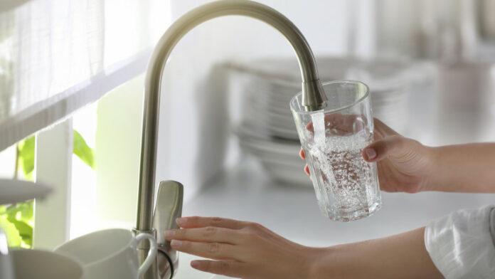 Woman pouring water into glass in kitchen, closeup