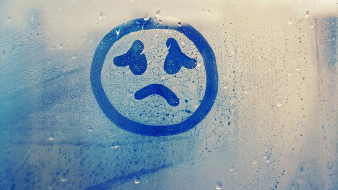 drawn sad face on foggy glass window raindrops blue color concept photo